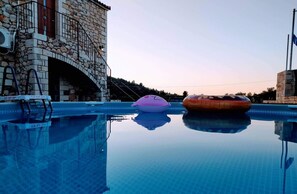 Piscina com dois flutuadores infláveis, um edifício de pedra e um céu limpo.