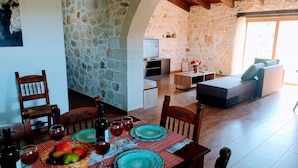 A cozy living space with stone walls, a dining area with a table set for a meal, and a comfortable seating area with a sofa and a TV. - Traditional Villa in Pemonia (Apokoronas)