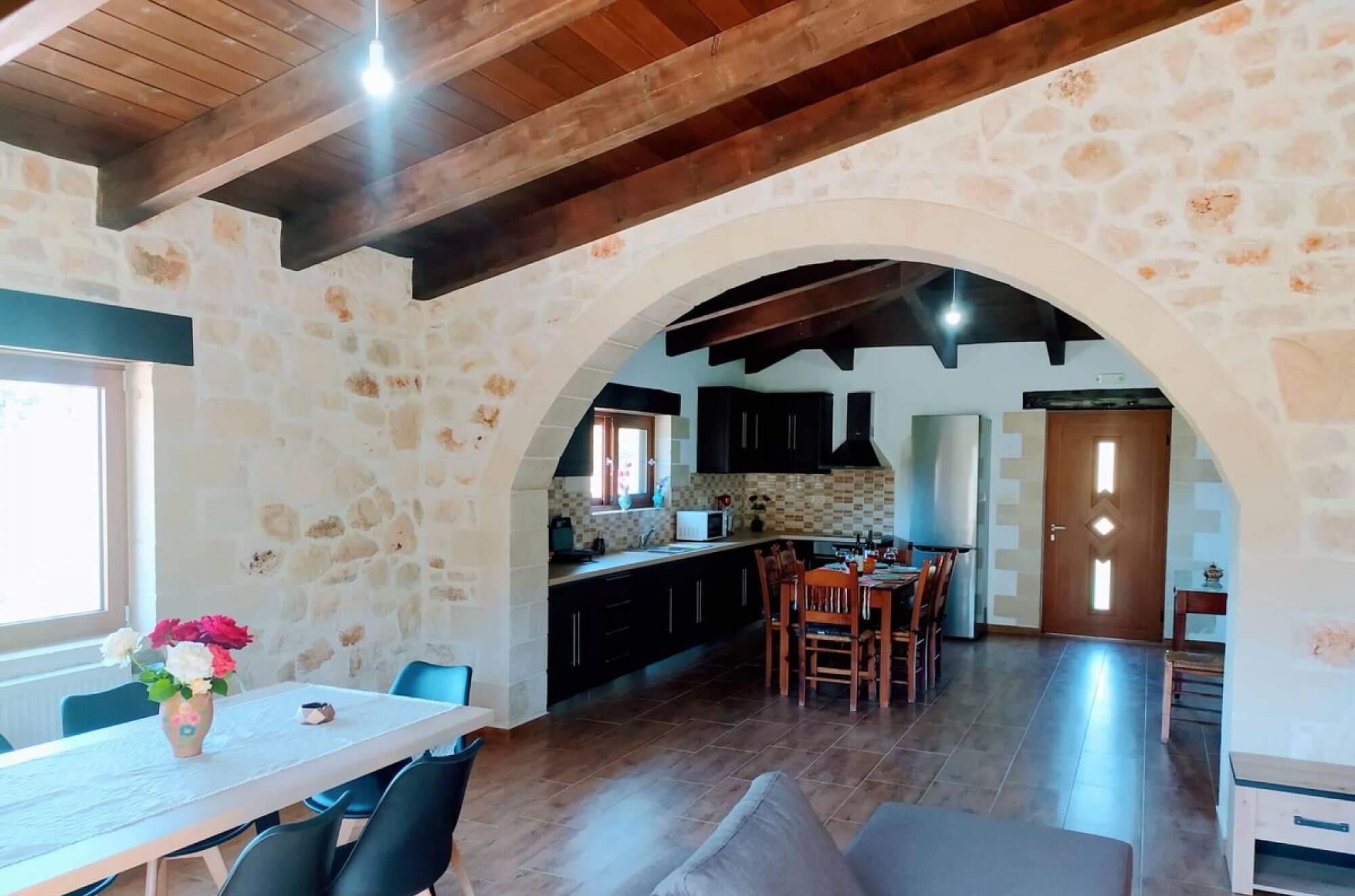 A spacious kitchen with a stone archway, wooden ceiling beams, and a dining area with a table and chairs.
