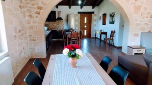 A dining area with a table set for four, a vase with flowers, and a view into the kitchen and living room through an archway. - Traditional Villa in Pemonia (Apokoronas)