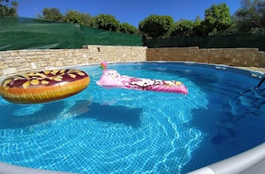 A swimming pool with two inflatable toys, one shaped like a donut and the other like a swan, surrounded by stone walls and a green cover. - Traditional Villa in Pemonia (Apokoronas)