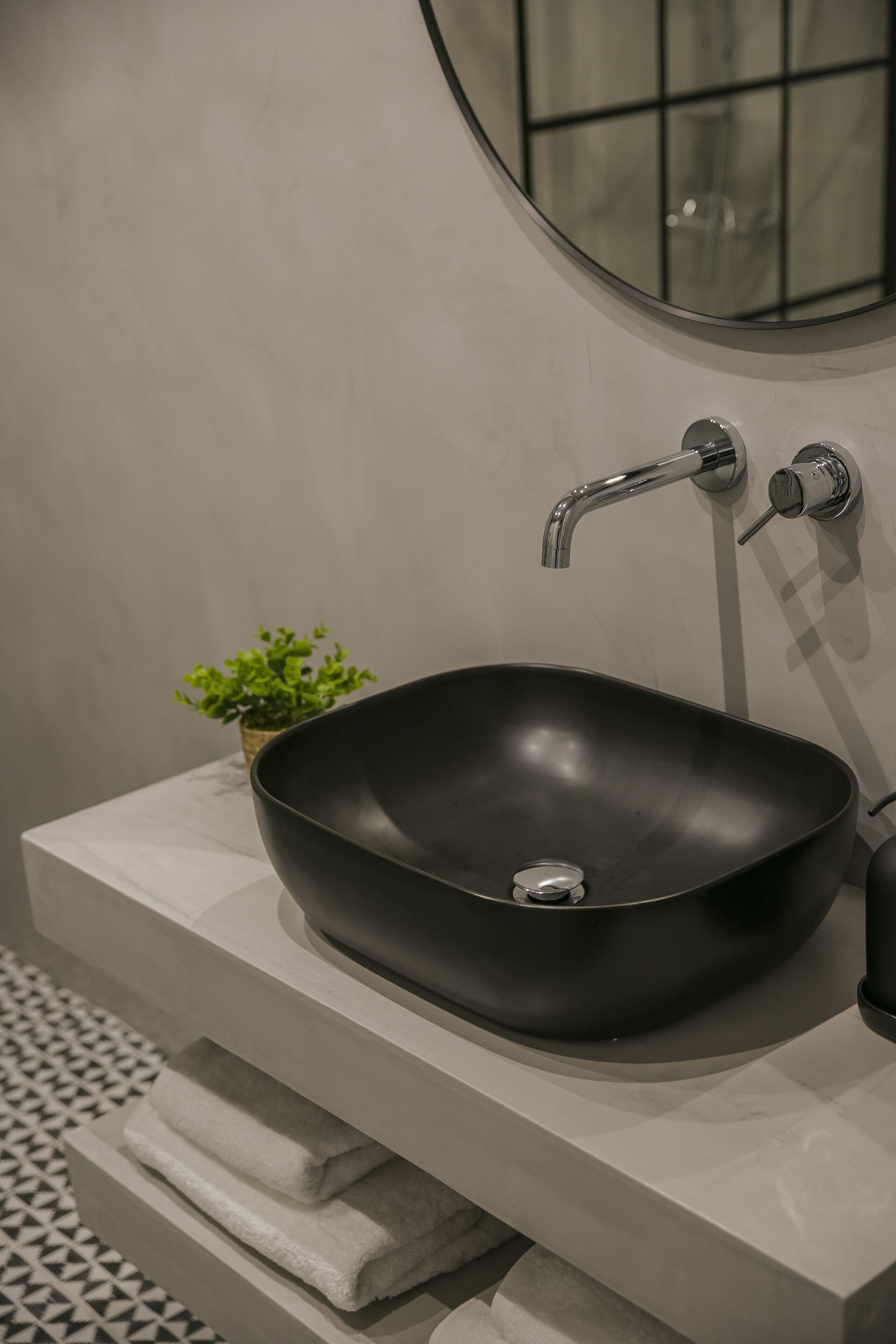 Een moderne badkamer met een zwart wastafel, een kleine plant in een pot en een spiegel boven de wastafel.
