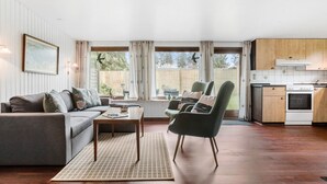 Una sala de estar acogedora con sofá, sillones, una mesa de centro y una zona de cocina con estufa y armarios.
