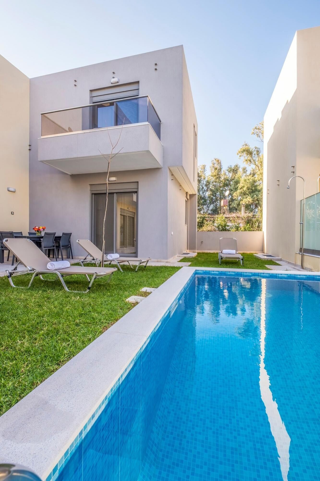 A modern house with a swimming pool, a dining area, and a lounge with sun loungers.