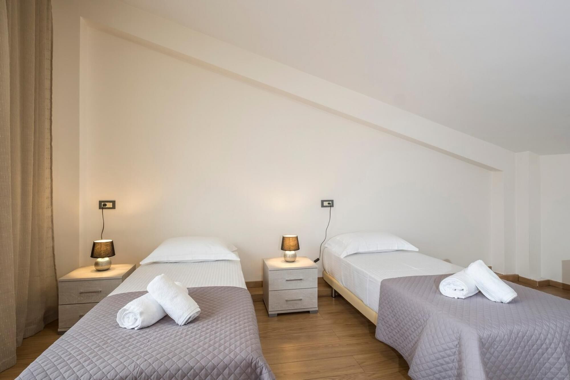 A hotel room with two single beds, each with a bedside table and lamp.