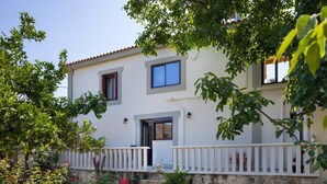 Une maison à deux étages, avec des fondations en pierre, une façade blanche et un balcon doté d’une balustrade blanche.