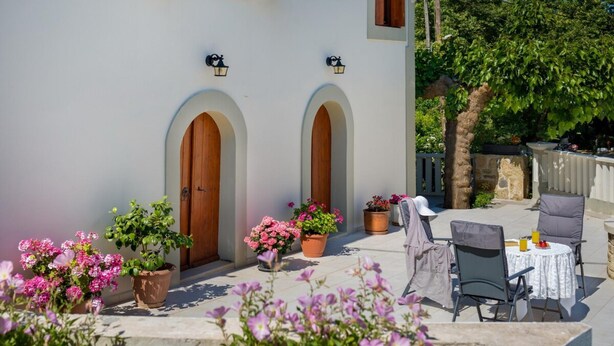 Un espace patio aménagé avec des meubles d’extérieur, des plantes en pot et un bâtiment blanc doté de portes en arc de cercle.