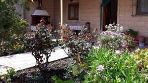 Ein Backsteinhaus mit einer gefliesten Terrasse, einem Schornstein und einem Garten mit verschiedenen Pflanzen und Blumen.