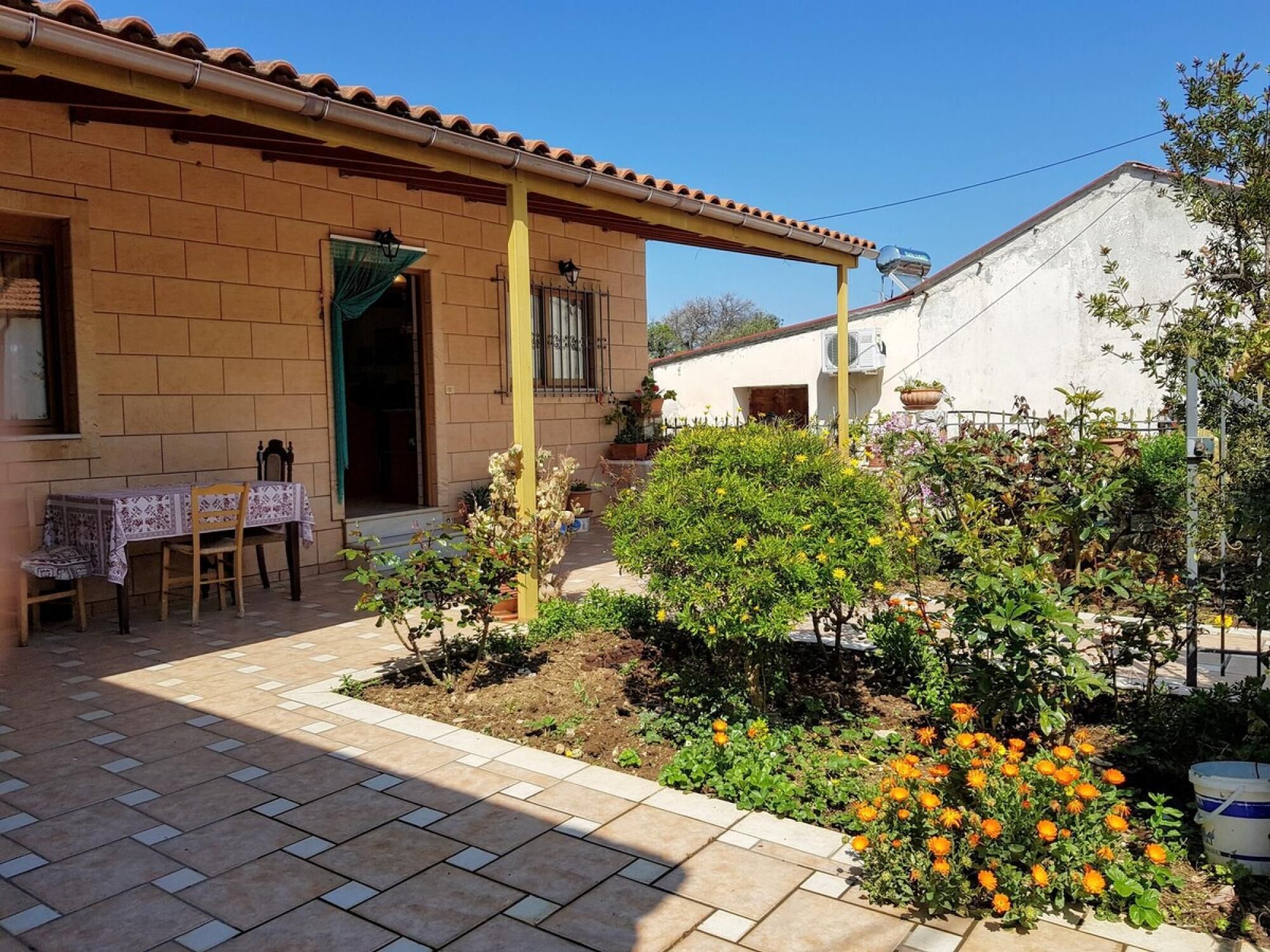Un cortile con un patio piastrellato, una zona salotto coperta e diverse piante e fiori.