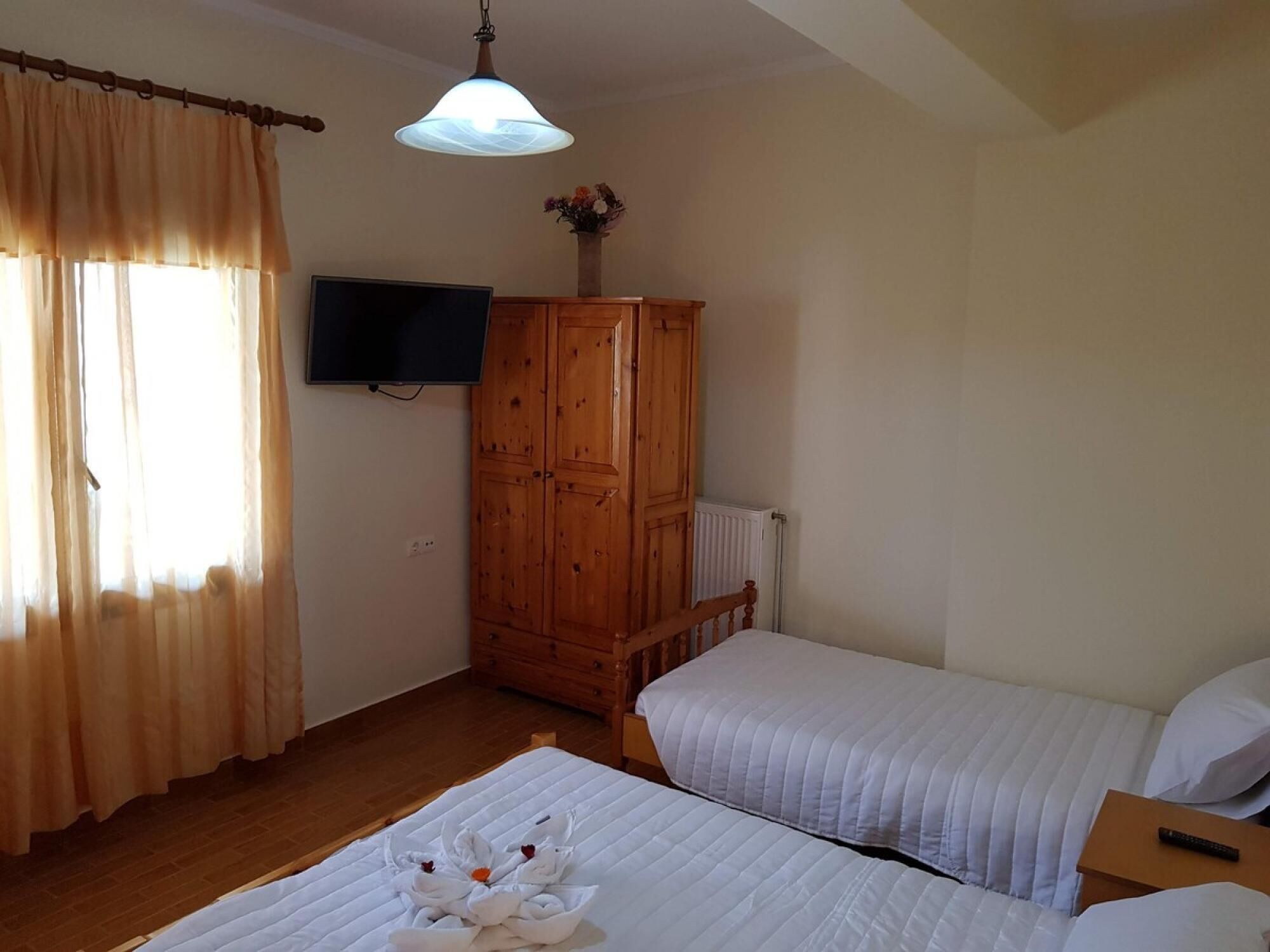 A bedroom with two beds, a wooden wardrobe, a television, and a radiator.