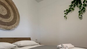 A hotel room with a large bed, two rolled white towels, a wooden headboard, a wall-mounted plant, and a textured wall hanging. - MATTEOTTO RESIDENCE, 2-BEDROOM APARTMENT, (Sardegna)