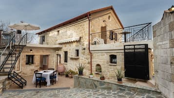 A stone building with a balcony, a table with chairs, and potted plants.