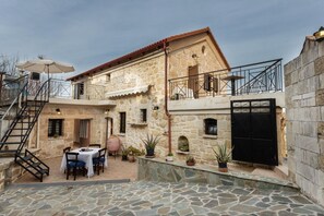 A stone building with a balcony, a table with chairs, and potted plants. - Traditional Stone House Rafael (Apokoronas)