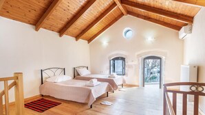 Un dormitorio con dos camas, suelo de madera, techo inclinado y vistas a través de un arco.