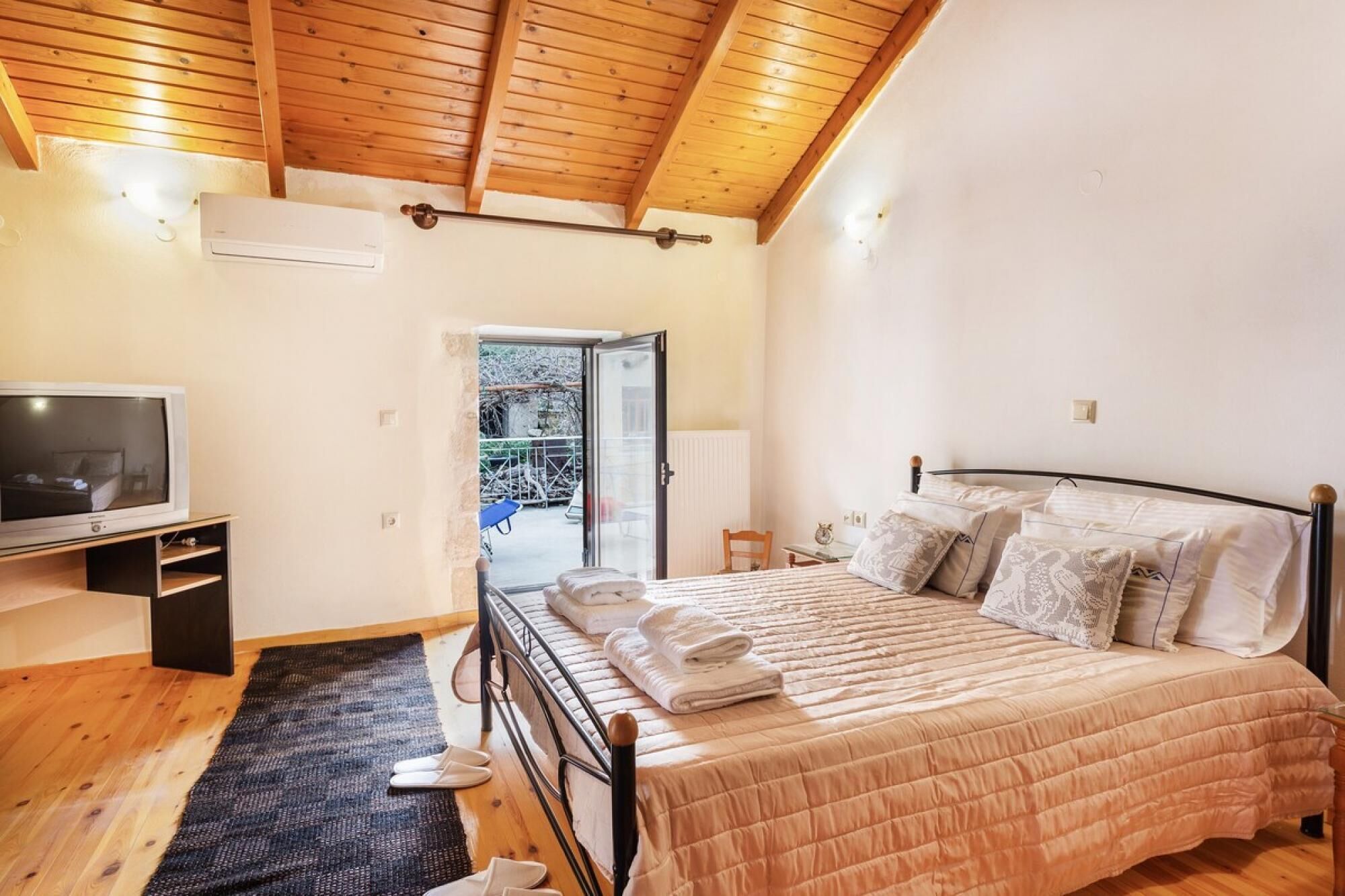 A bedroom with a bed, a TV, and a wooden ceiling.