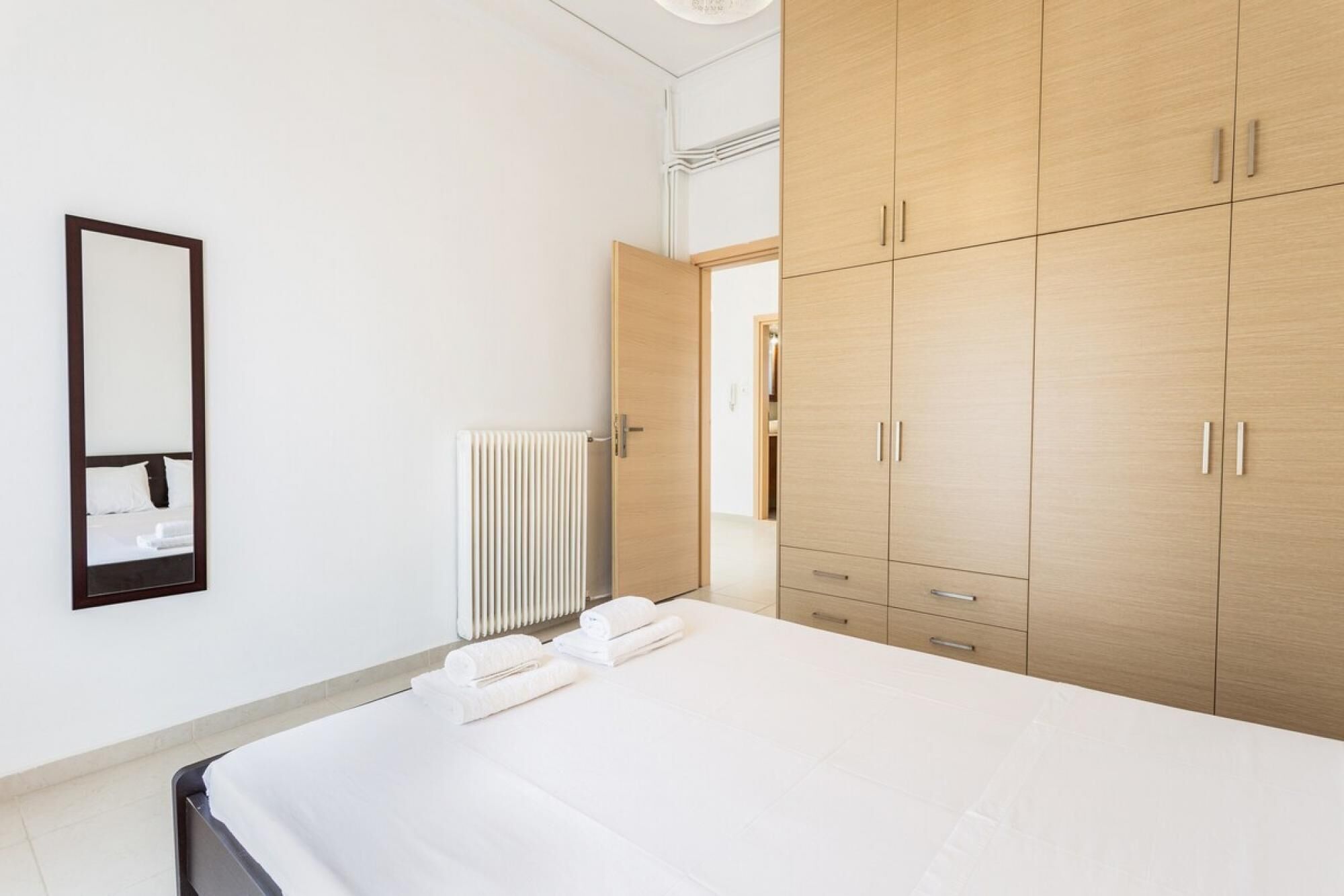 A hotel room with a large bed, a wooden wardrobe, a radiator, and a mirror on the wall.