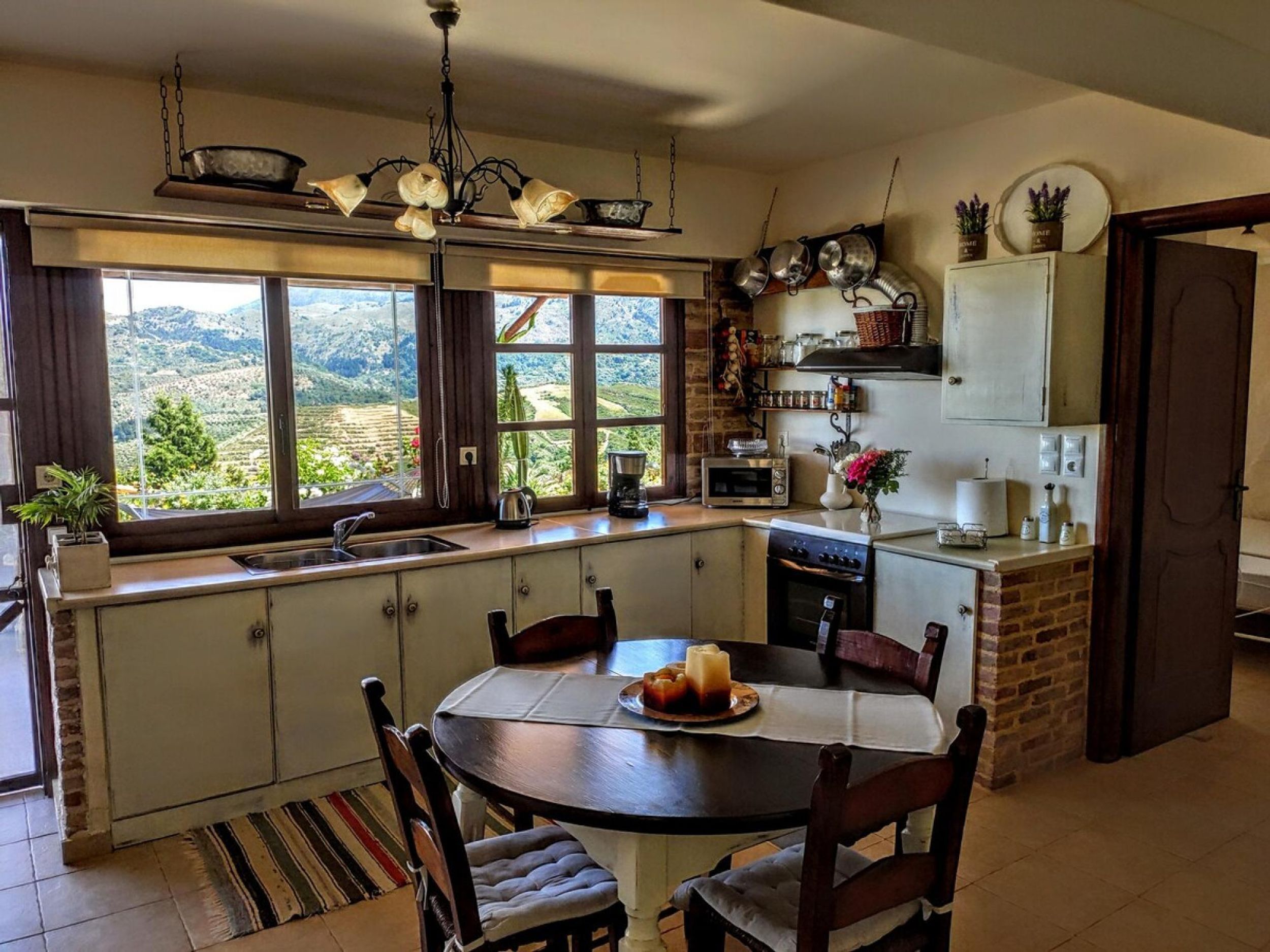 A kitchen with a central island, a dining table, and a view of a mountainous landscape through large windows.