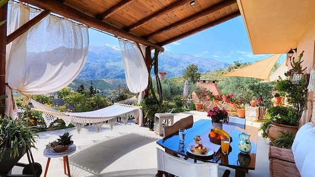 Un espace extérieur aménagé, abrité et doté de tables préparées pour le petit-déjeuner, entouré de plantes en pot et offrant une vue sur les montagnes.