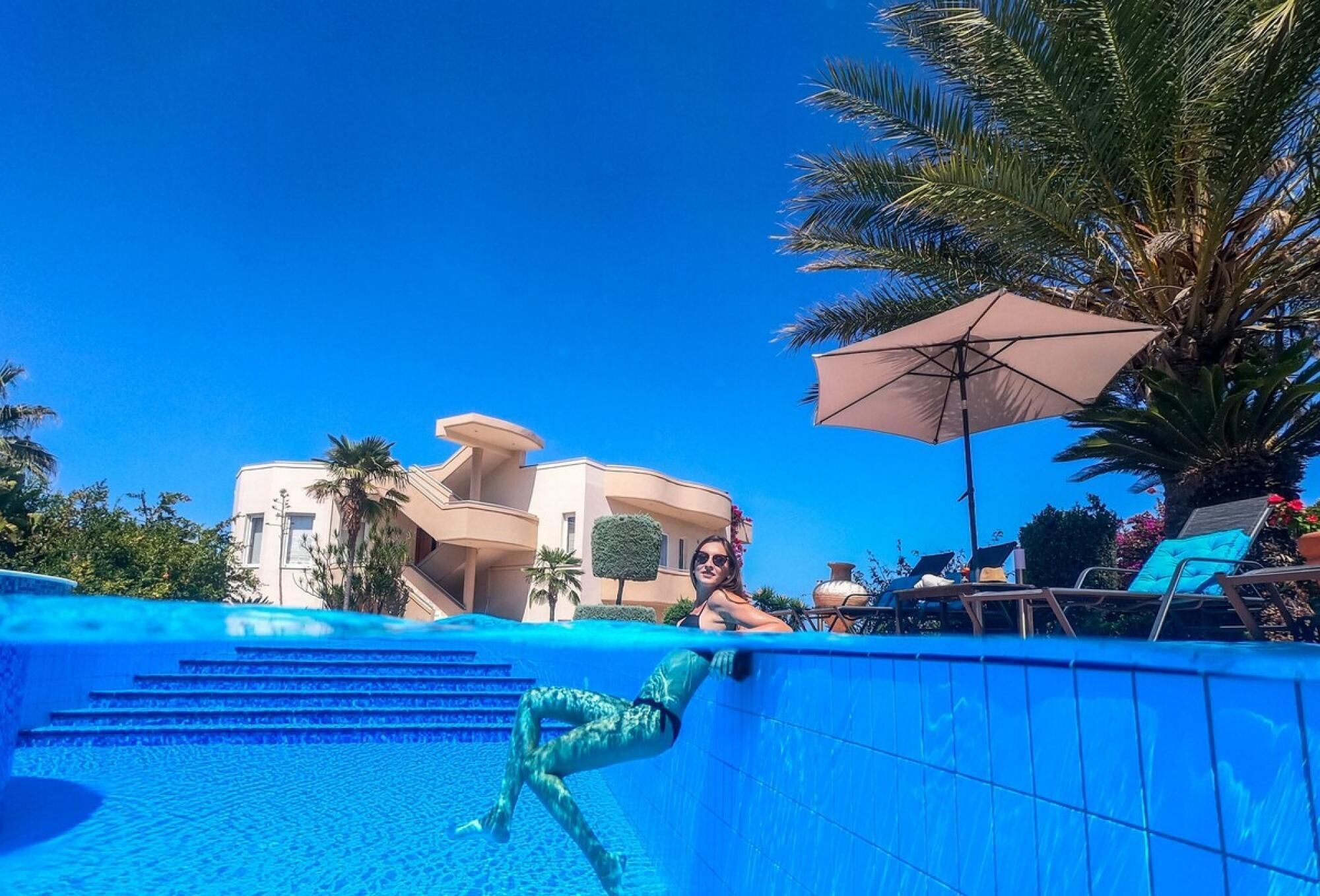 Une piscine avec des marches descendant vers l’eau, entourée de palmiers et de chaises longues.