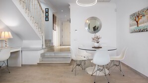 Uma área de refeições moderna com uma mesa redonda, cadeiras brancas e um lustre.