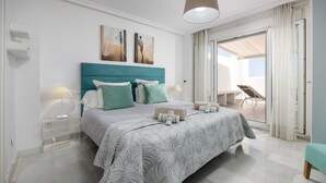 Quarto moderno com cama grande, cabeceira verde-água e varanda com espreguiçadeira.