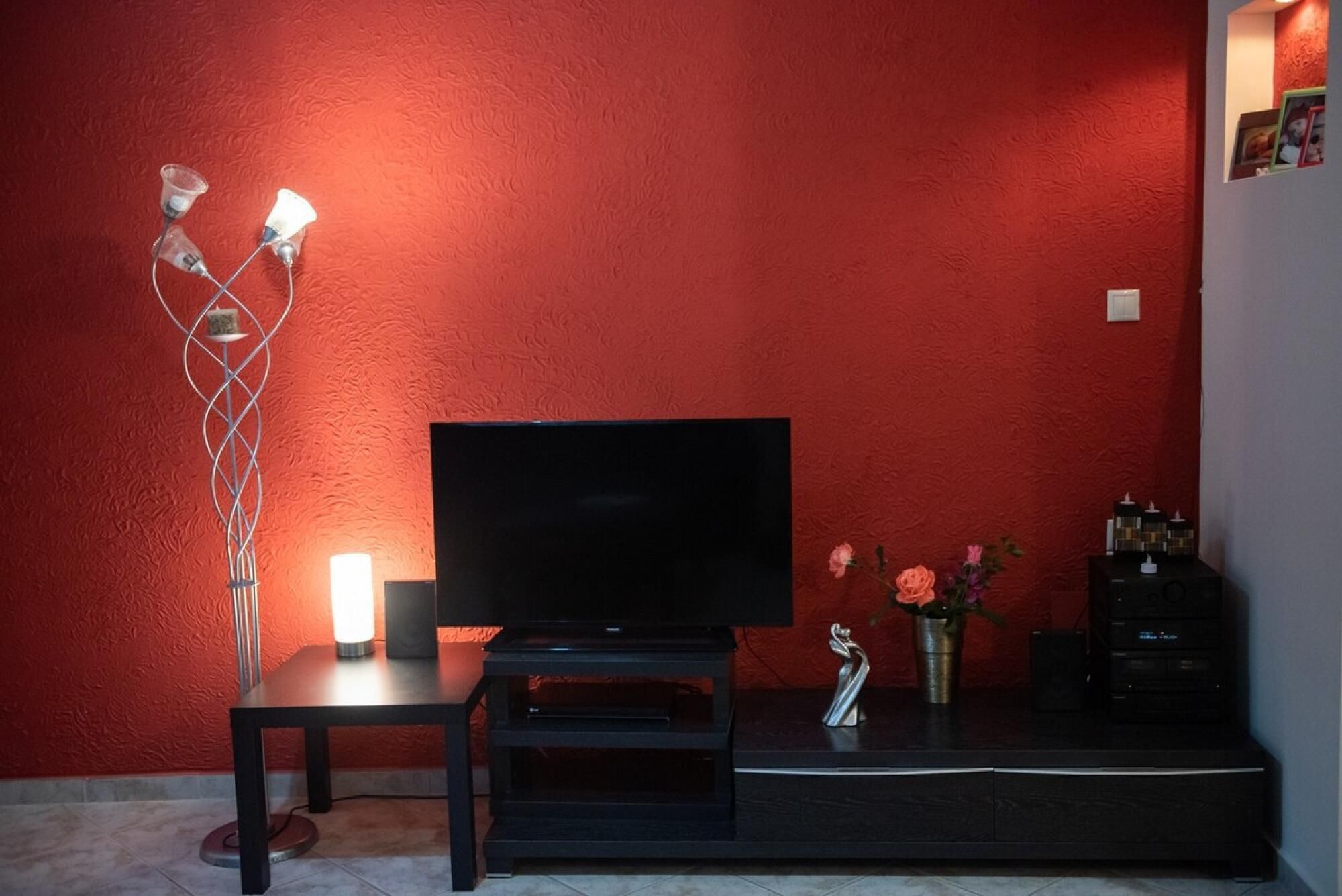 A living room with a TV on a stand, a floor lamp, a vase with flowers, and a small statue on a console table.