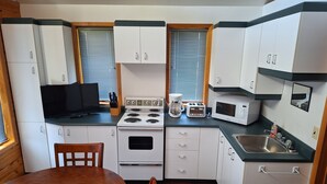 A compact kitchen with white cabinets, a stove, a microwave, and a toaster. There is a dining table with chairs and a TV on the counter. - The West Arm Getaway
STRSTC-2026-03 (St.-Charles)