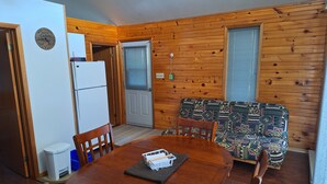 A compact kitchen with a refrigerator, a dining table with chairs, a patterned sofa, and a clock on the wall. - The West Arm Getaway
STRSTC-2026-03 (St.-Charles)