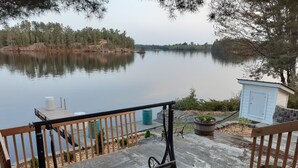 A wooden bench overlooking a calm lake with a small shed and potted plants nearby. - The West Arm Getaway
STRSTC-2026-03 (St.-Charles)