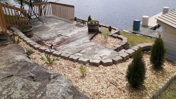 A lakeside patio with a wooden deck, a bench, and a small garden area with potted plants. - The West Arm Getaway
STRSTC-2026-03 (St.-Charles)