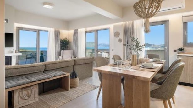 Una sala de estar moderna con una mesa de comedor de madera, un banco empotrado y grandes ventanales con vistas al mar.