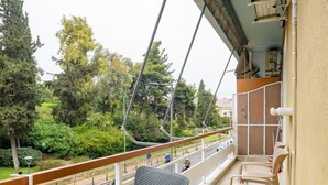 A balcony with a chair and a table, overlooking a road and greenery.