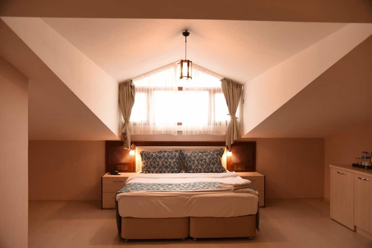 A bedroom with a sloped ceiling, a bed with patterned pillows, bedside lamps, and a window with sheer curtains.