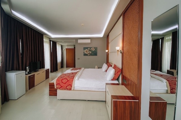 A modern hotel room with a large bed, a TV, a minibar, and a wooden accent wall.
