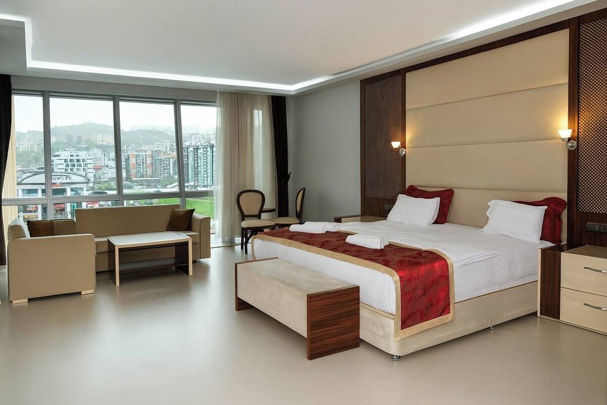 A modern hotel room with a large bed, a sofa, a small table, and a view of the city.