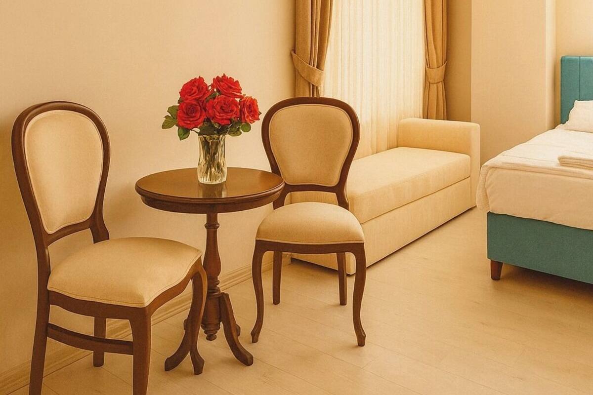 A hotel room with a bed, two chairs, a small table with a vase of flowers, and a sofa.