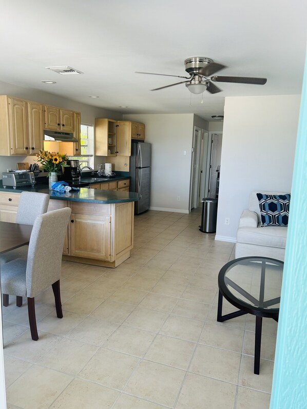 A modern kitchen with wooden cabinets, a stainless steel refrigerator, and a dining area with a table and chairs. - Direct panoramic waterfront views (Marco Island)