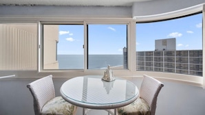 A balcony with a glass table and two chairs, overlooking the sea.