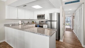 A modern kitchen with white cabinets, granite countertops, stainless steel appliances, and a sign reading "BEACH HOUSE". - Ocean Princess-Beautiful 2 Bedroom Condo! (Ocean City)