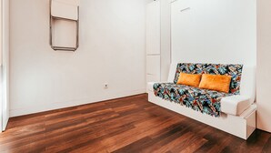 A minimalist room with a white sofa, a wooden floor, and a large window. - Studio S. José By Gt House (Lisbon)