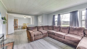 Un vaste salon doté d’un grand canapé d’angle, d’un coin repas avec une table et des chaises, et offrant une vue sur l’extérieur grâce à de grandes fenêtres.