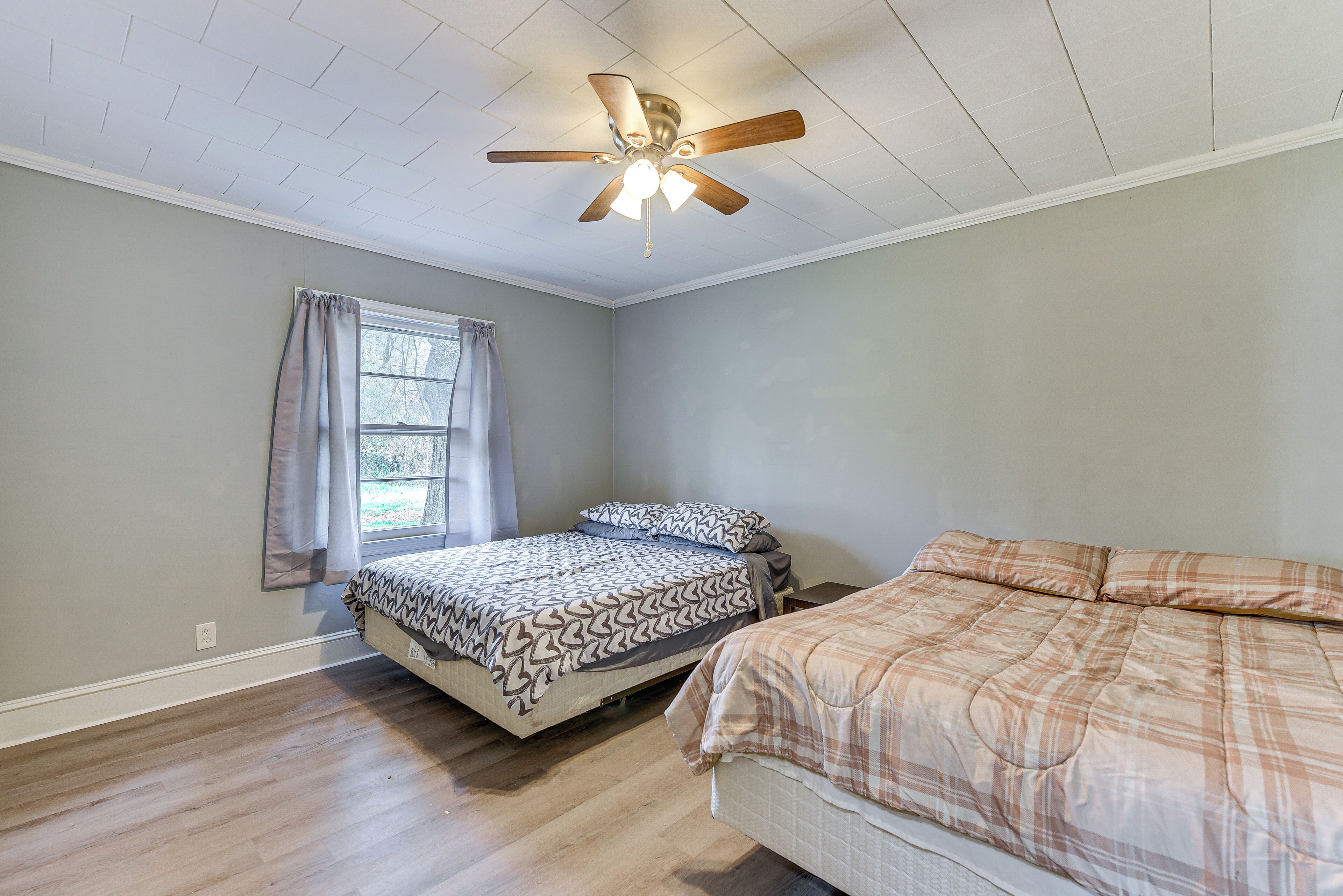 Une chambre avec deux lits, un ventilateur de plafond et une fenêtre avec des rideaux.