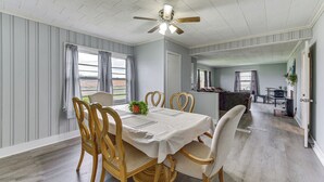 Un coin repas avec une table dressée pour quatre personnes, des chaises en bois, un ventilateur de plafond et une vue par la fenêtre.