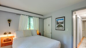 Un dormitorio con una cama grande, una mesita de noche con lámpara, una ventana con cortinas y un cuadro enmarcado en la pared.