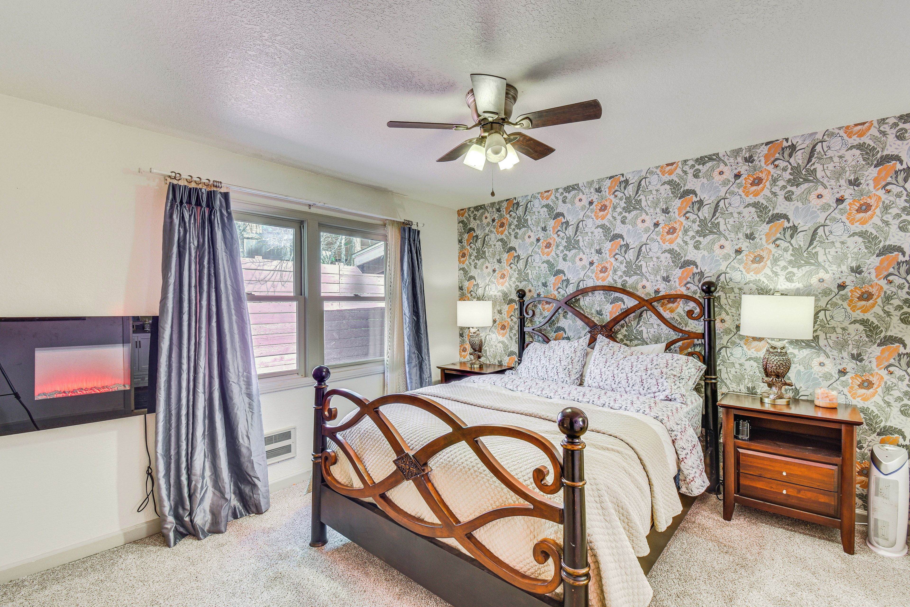 A bedroom with a bed, a ceiling fan, a nightstand, a lamp, and a wall with floral wallpaper.