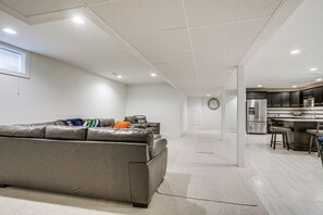 A modern living room with a gray sectional sofa, a kitchen area with stainless steel appliances, and a large clock on the wall. - Convenient North Bend Apt: Half-mi to Notre Dame! (South Bend)