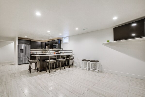 A modern kitchen with a central island, bar stools, and a flat-screen TV mounted on the wall. - Convenient North Bend Apt: Half-mi to Notre Dame! (South Bend)