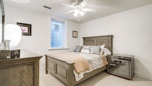 A bedroom with a wooden bed, a nightstand, a dresser, a ceiling fan, and a window with blinds.