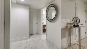 A hallway with white walls, a marble floor, a round mirror, and a door leading to a bathroom.