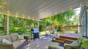 Een overdekt terras met rieten meubels, een barbecue en uitzicht op het omliggende groen.